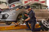 Jiffy Lube technician using a flashlight to visually inspect the brake pad of a silver electric car