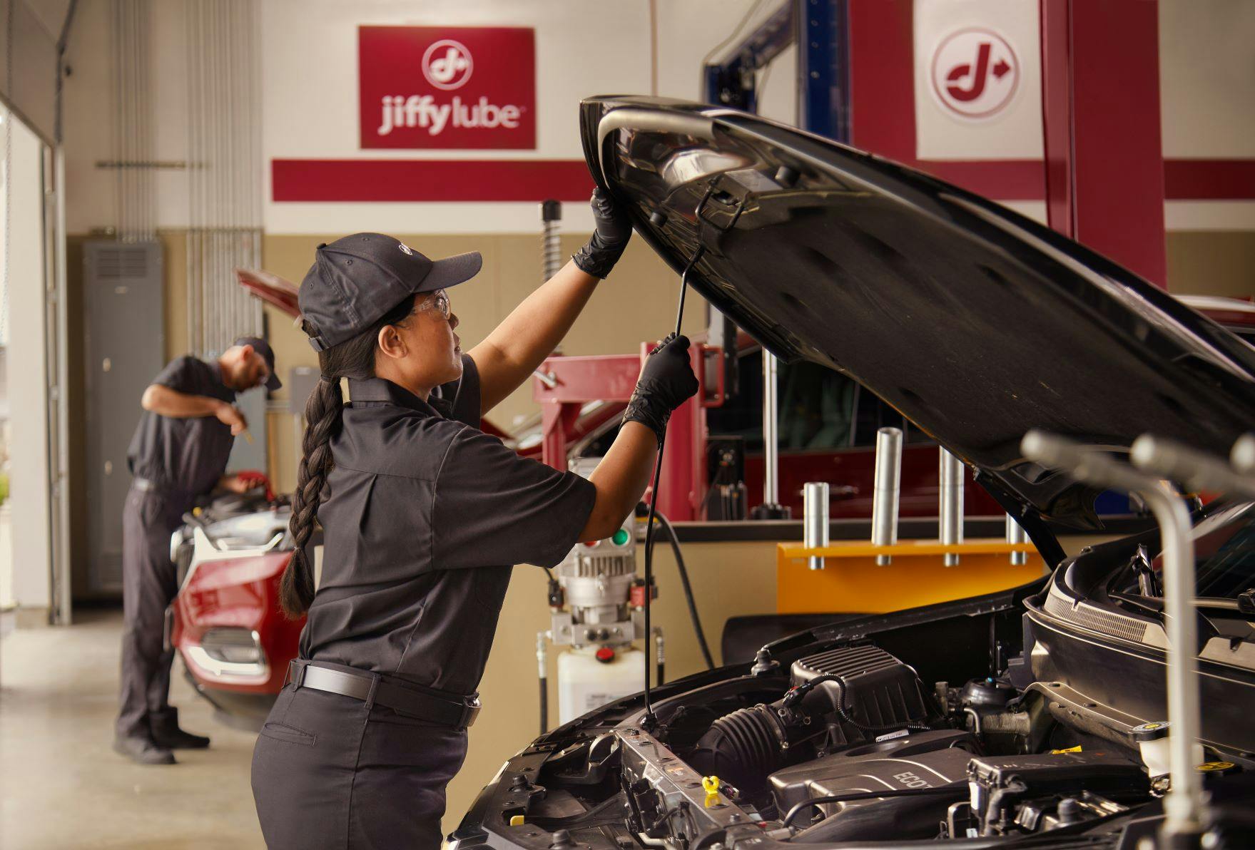 Jiffy Lube technician propping up a vehicle hood before inspecting the car's alternator 