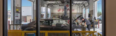 Technician servicing a car with its hood open inside a service bay