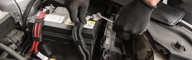 A Jiffy Lube technician wearing black gloves performing battery services on a car battery terminal