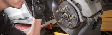 A Jiffy Lube technician wearing safety goggles servicing a vehicle's brake router with small flashlight