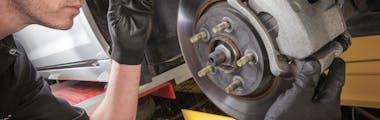 Jiffy Lube technician visually inspecting the brake pad of a silver car