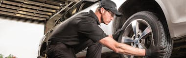 Jiffy Lube technician wearing all black uniform replacing a tire after balancing the wheel