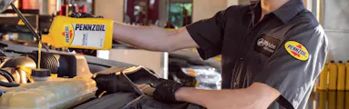 Technician adding motor oil to a vehicle during an oil change