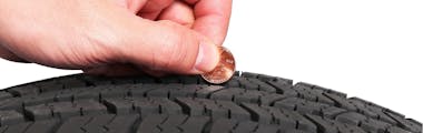 hand holding a penny close to a tire to show tire tread depth