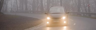 Halogen headlight of a sedan vehicle shining through light misting rain