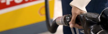 Woman's hand holding a fuel nozzle while pumping gas at a Shell gas station