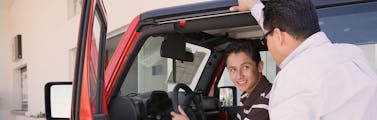 Father stands outside the driver side door and gives his son new driver tips about the red Jeep the son is learning to drive