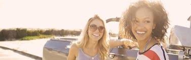 Two women standing next to a truck discussing summer car care tips with sun shining behind them