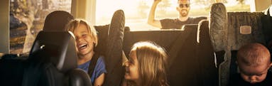 Three kids sitting and laughing in the backseat of a minivan as the father closes the trunk behind them