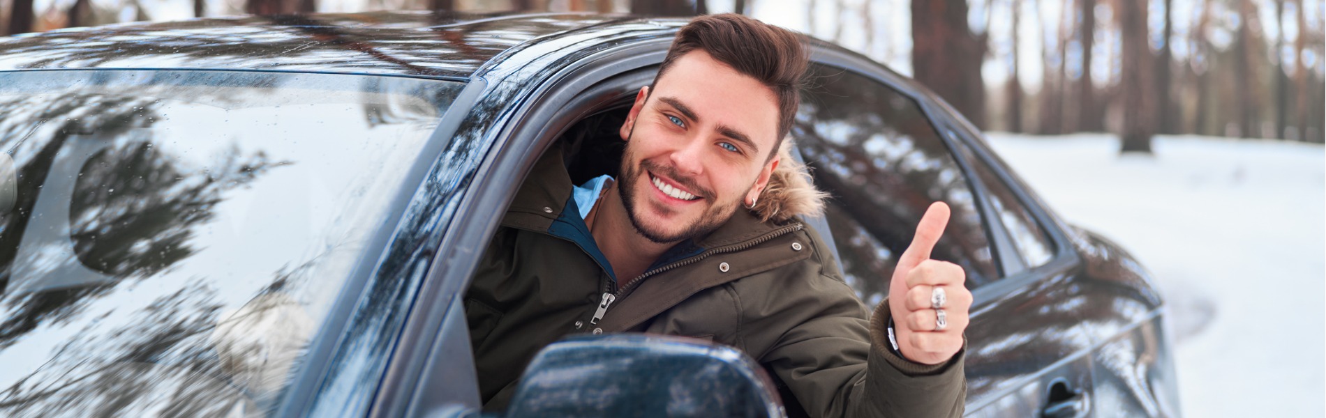 Man wearing winter coat giving thumbs up and smiling out the window in a snowy landscape